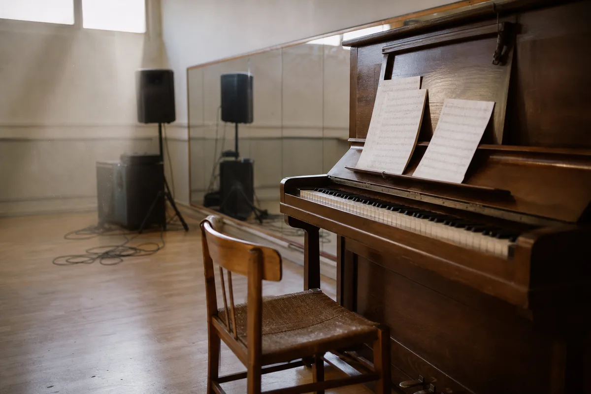Salle de répétition d’un théâtre avec une chaise vide et un piano droit sous la lumière de scène
