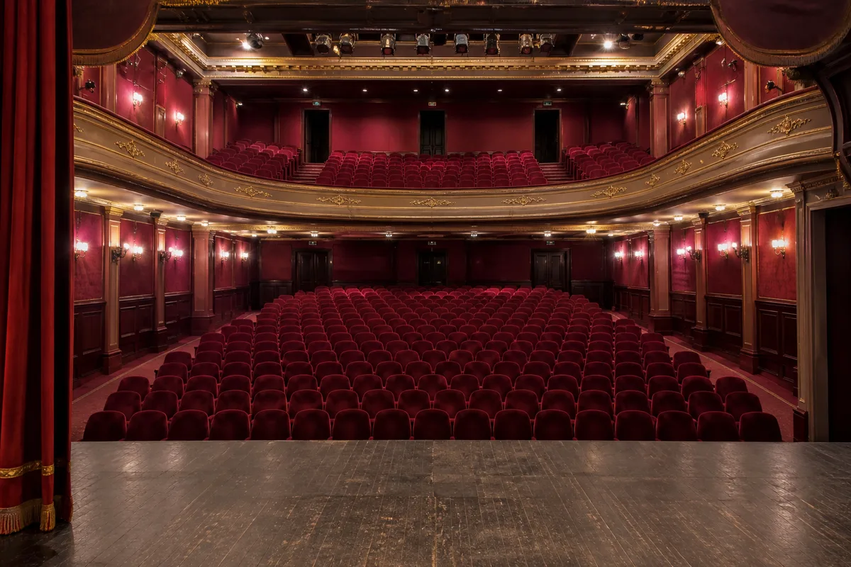 Rangées de sièges rouges vides vues depuis la scène d’un théâtre de ville, rideau ouvert, éclairage de service allumé